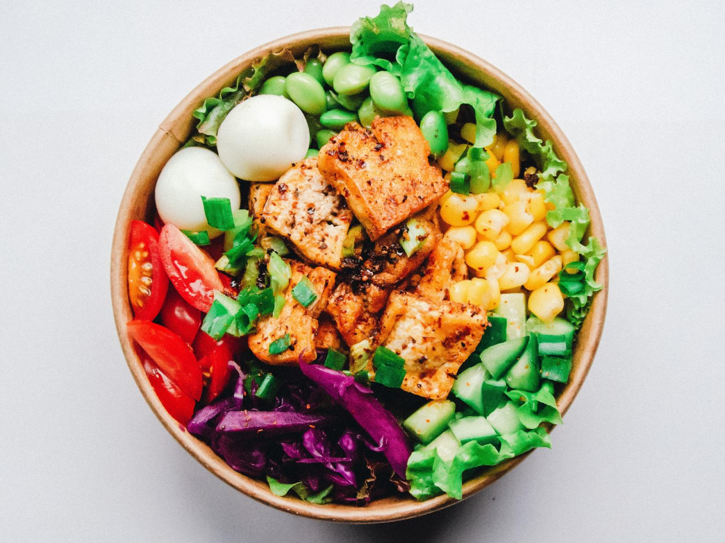 A colorful vegetarian protein bowl with tofu, greens, corn, tomatoes, and eggs.