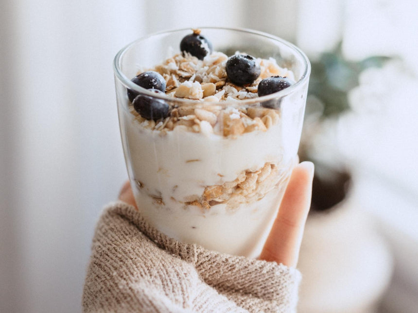 A hand holding a yogurt parfait with granola and blueberries