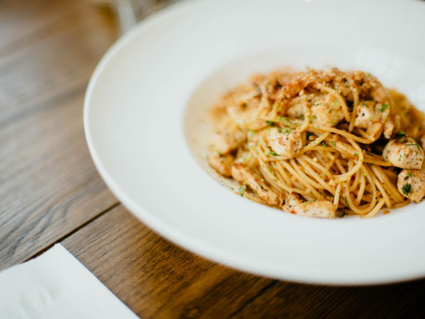 Angel hair pasta with chicken and herbs in a wide white bowl on a wooden table