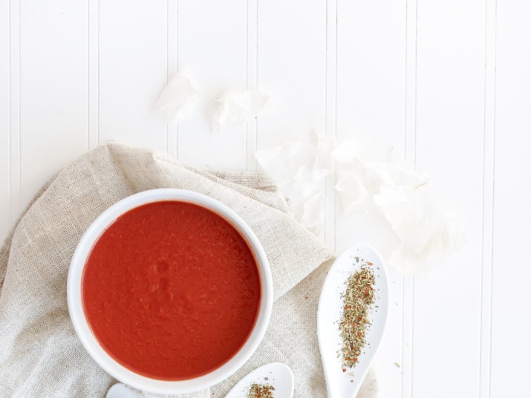Bowl of tomato soup with herbs on a white table