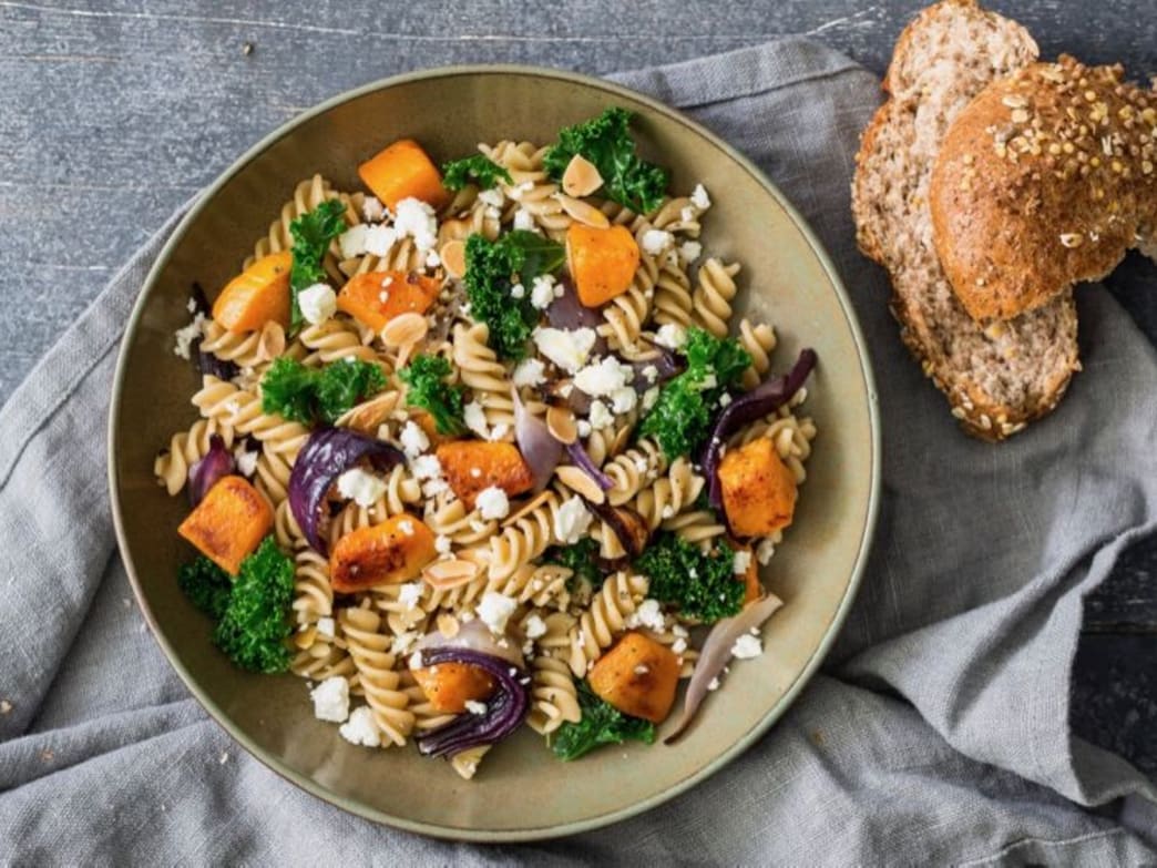 Whole wheat pasta salad with pumpkin, kale, feta, and almonds on a plate