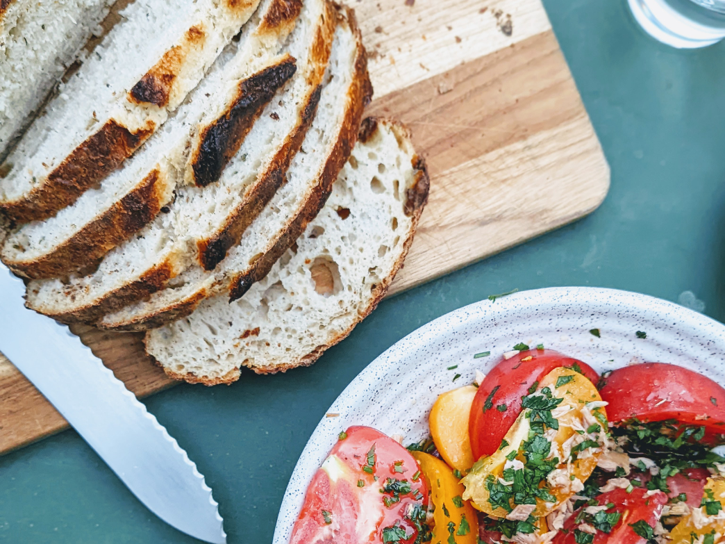 Sliced bread on a cutting board next to a colorful salad in a bowl