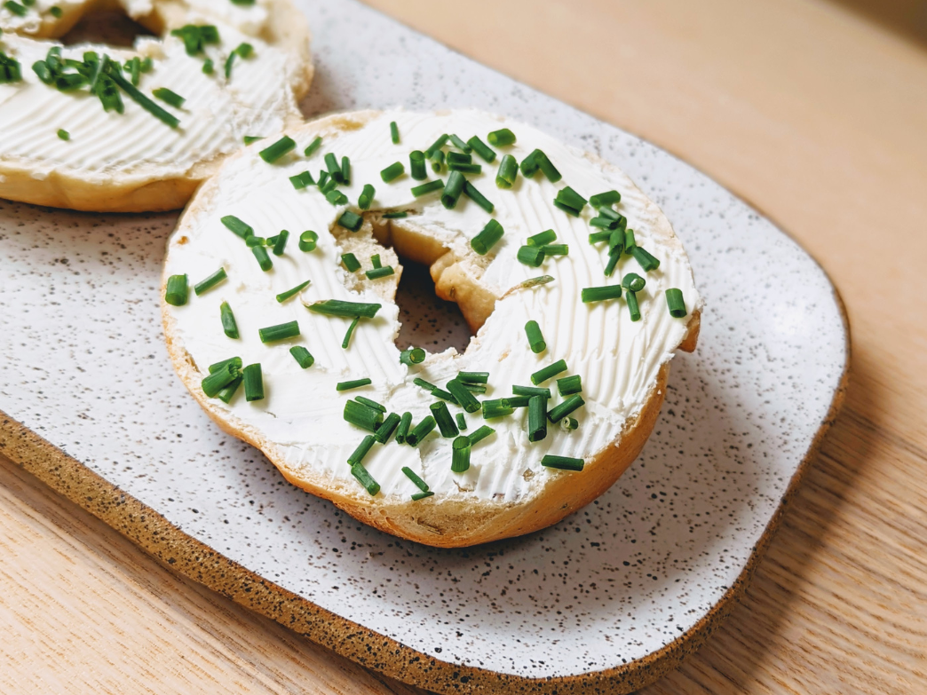 A bagel topped with cream cheese and chopped chives on a speckled plate.