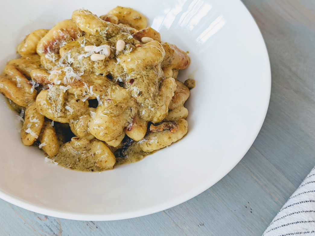 A bowl of gnocchi with pesto sauce and grated cheese on top.