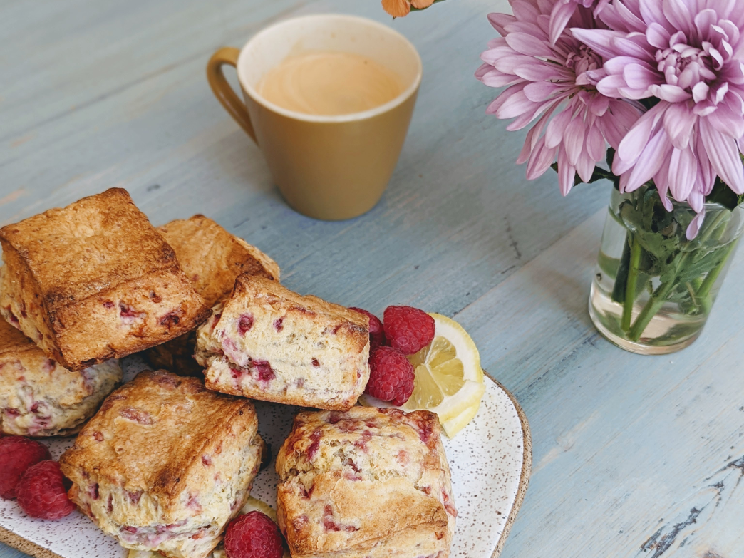 A plate of raspberry biscuits with fresh raspberries, a lemon slice, and a cup of coffee.