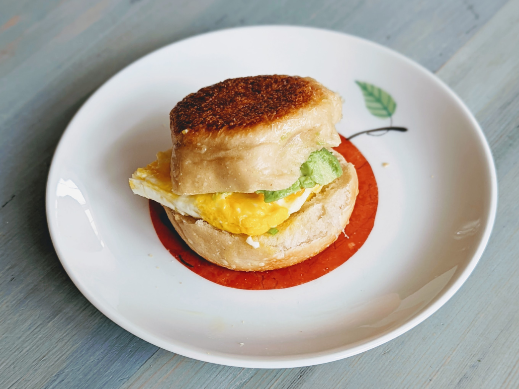 A toasted English muffin sandwich with egg and avocado on a plate.