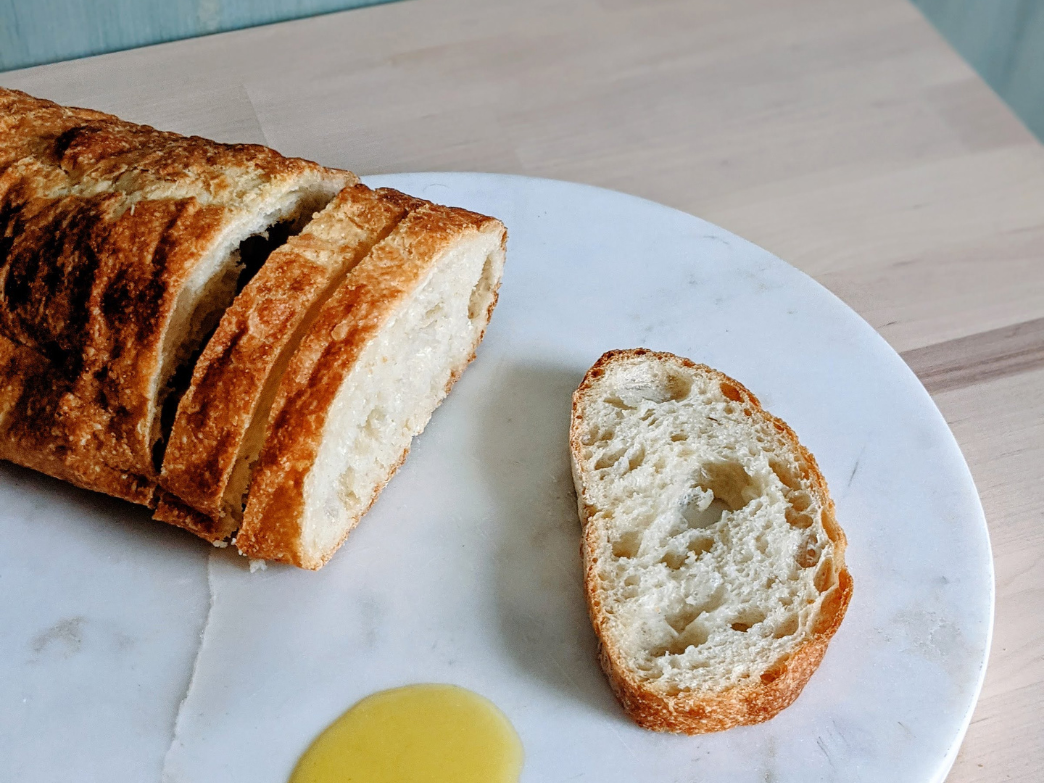 A sliced loaf of ciabatta bread on a marble surface with a piece of bread and olive oil.