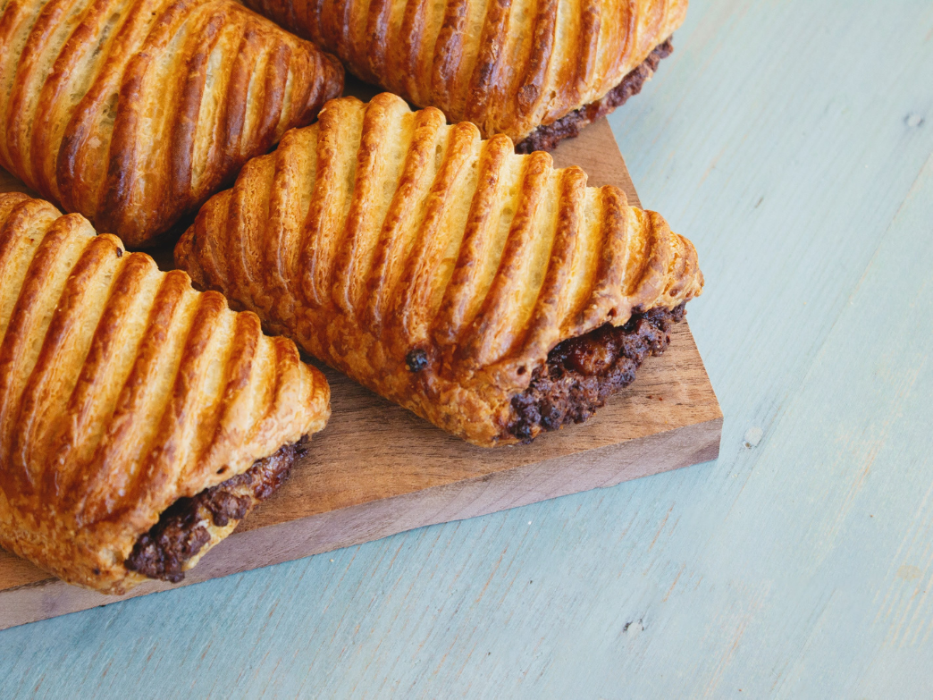 Four chocolate croissants on a wooden board, showcasing their flaky texture.