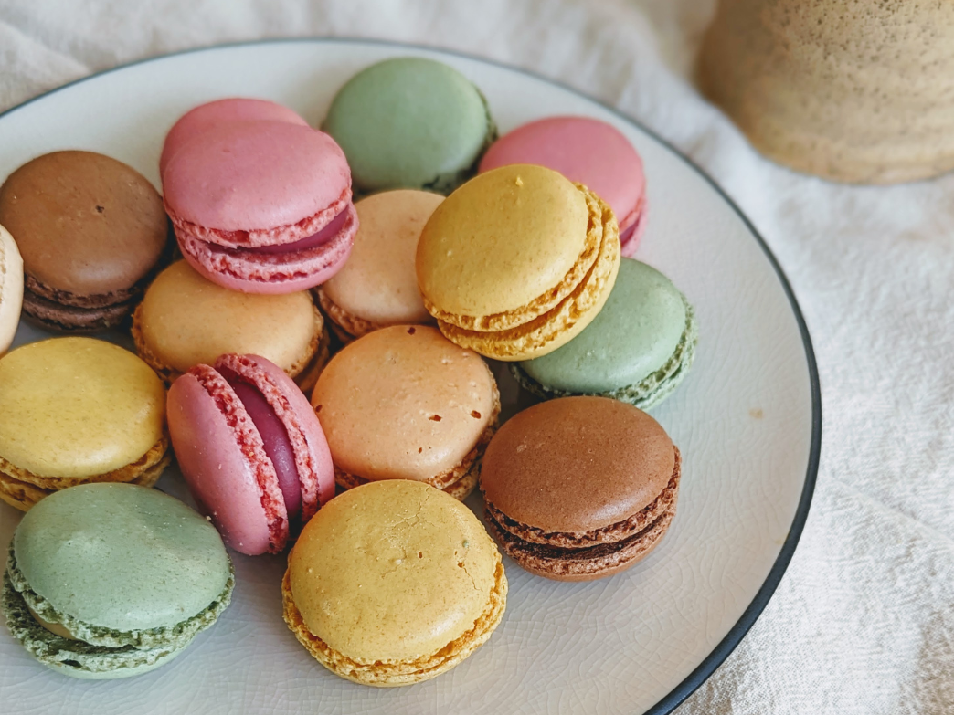 A plate of colorful macarons in various flavors including pink, green, yellow, and brown.