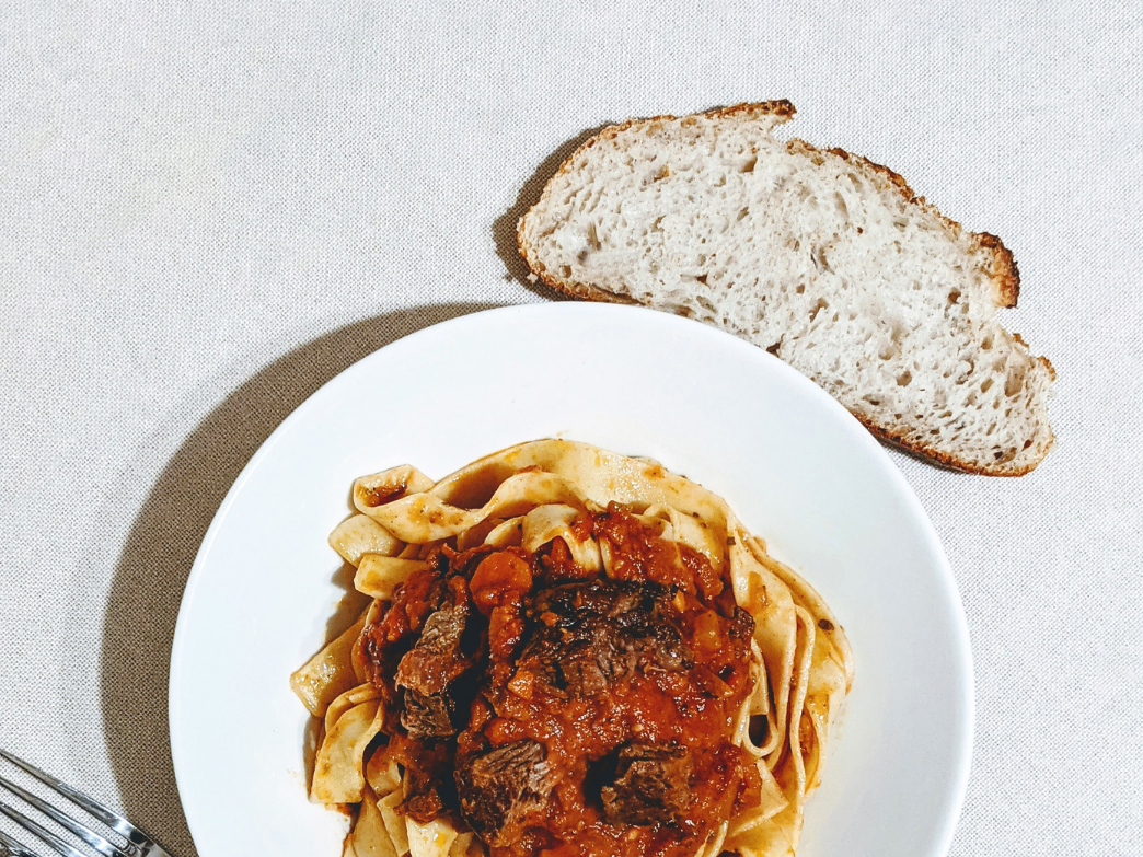 A plate of fettuccine with meat sauce and a slice of bread on the side