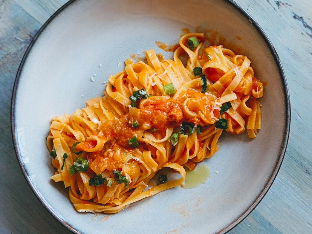 A plate of fettuccine pasta topped with tomato sauce and green onions.