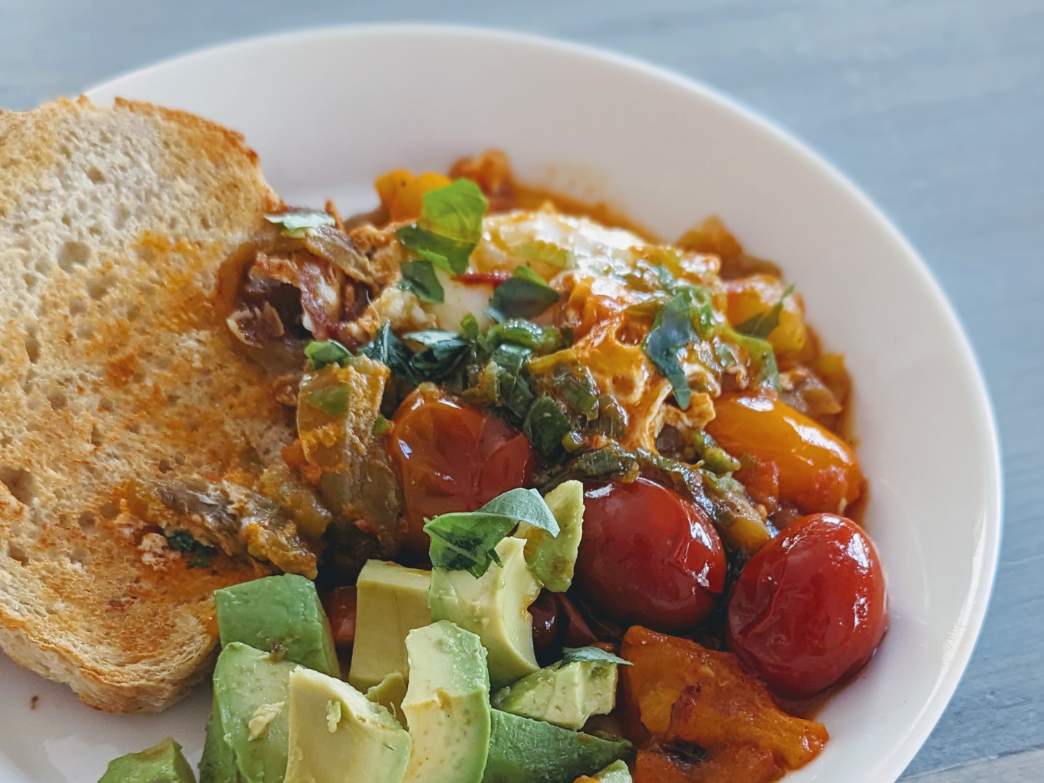 Toast, diced avocado, roasted cherry tomatoes and herbs in a white shallow bowl