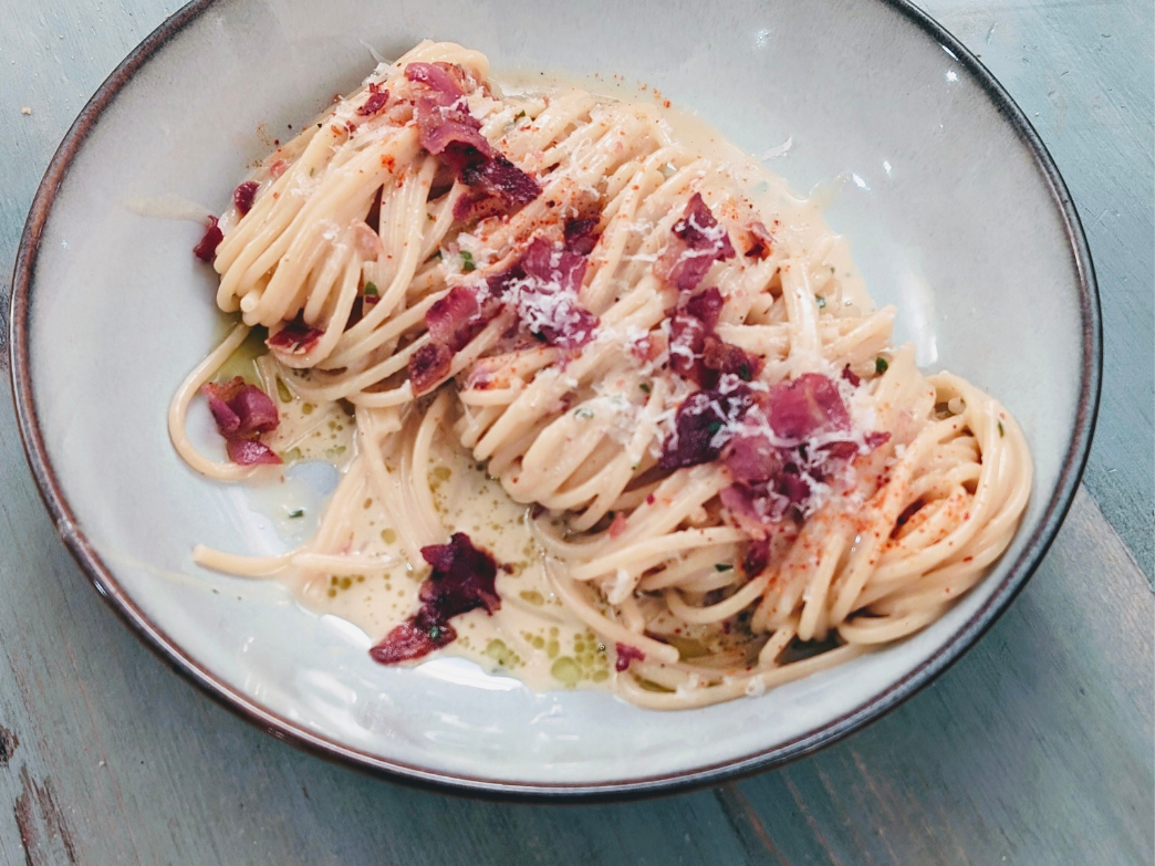 A plate of spaghetti topped with bacon bits and cheese.