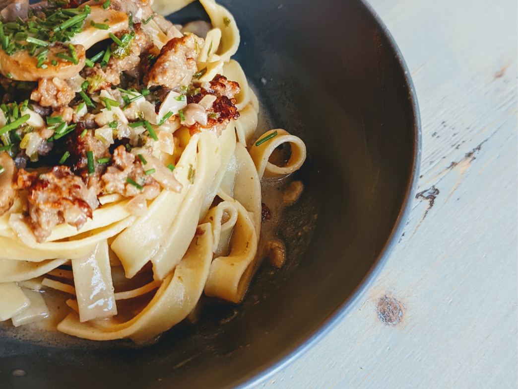 A close-up of fettuccine pasta topped with meat and herbs in a black bowl.