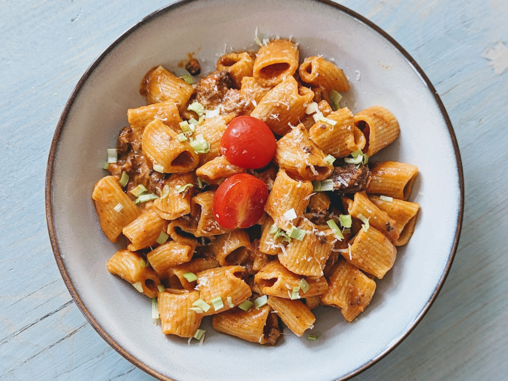 A bowl of pasta with cherry tomatoes and herbs on a blue surface
