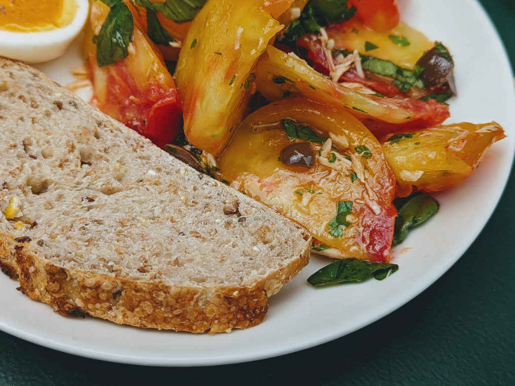 A plate with a slice of whole grain bread and a colorful salad of tomatoes and greens.