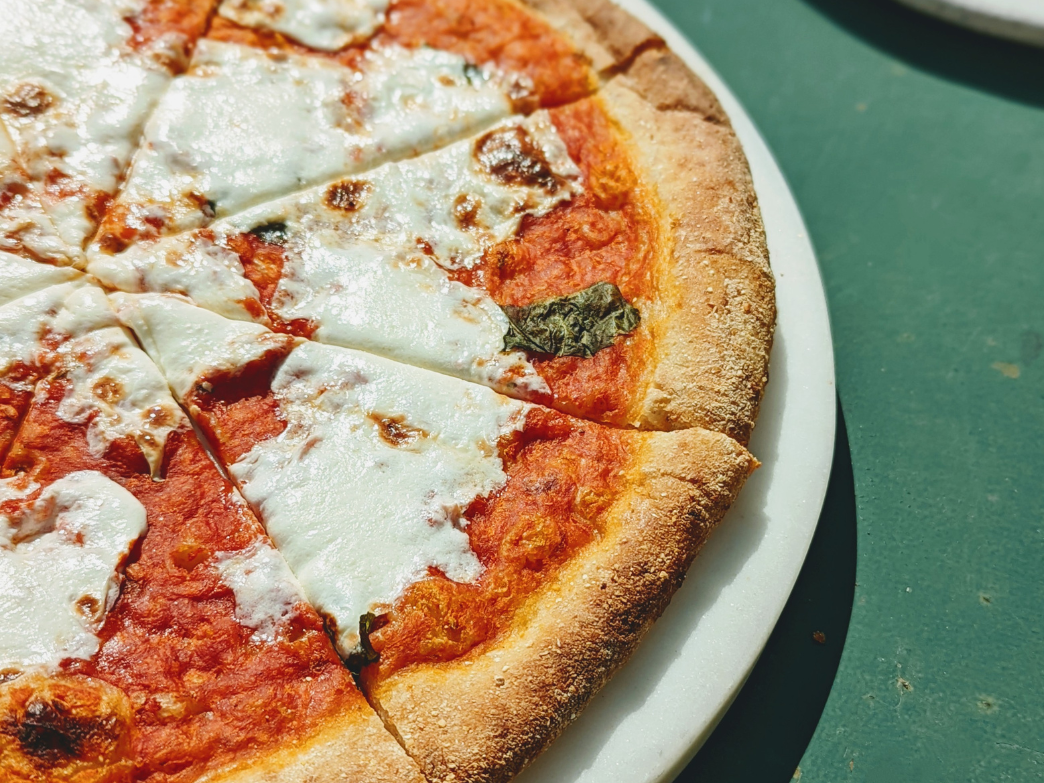 A close-up of a sliced pizza with melted cheese and tomato sauce on a green table.