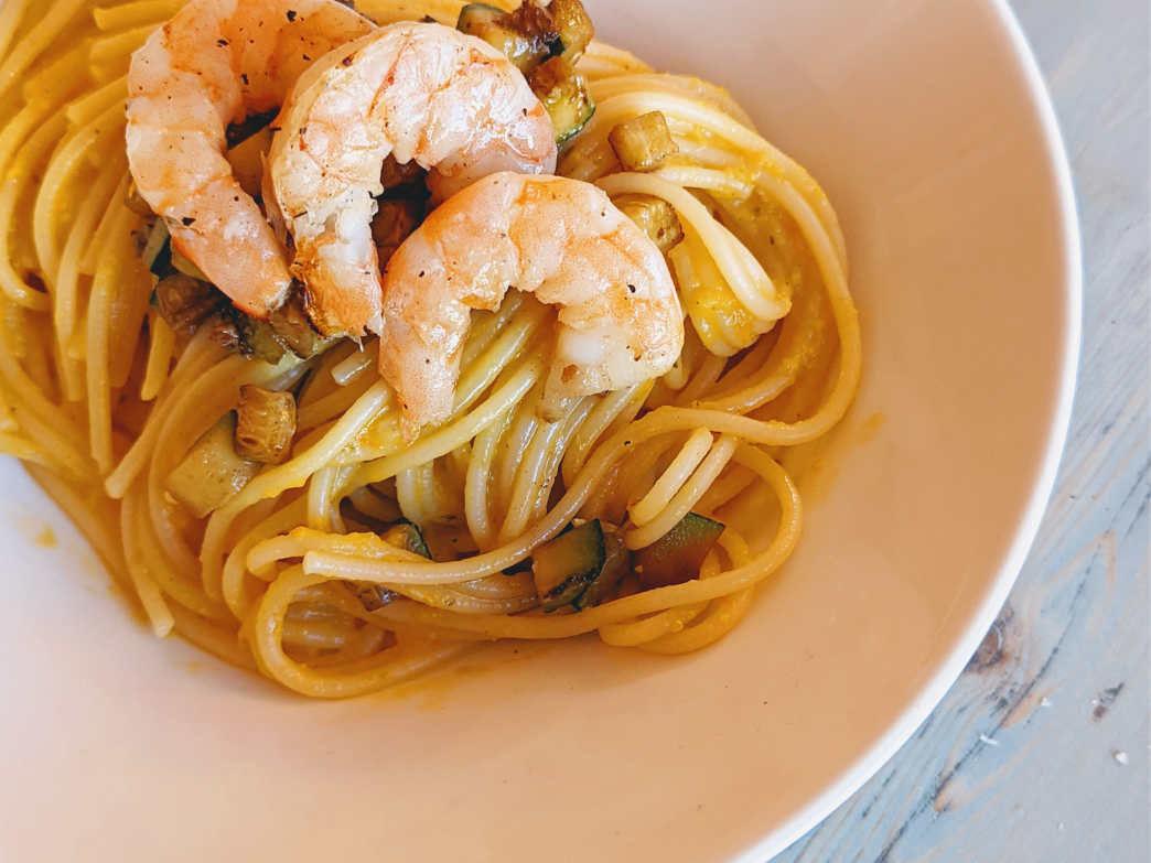 A bowl of pasta with shrimp and vegetables.