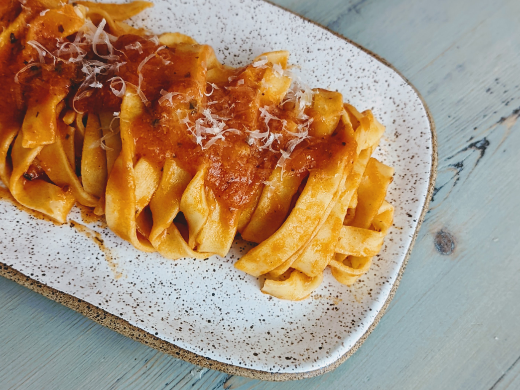 Close-up of fresh ribbon pasta with tomato sauce and grated cheese on a speckled rectangular plate on a light blue wooden table