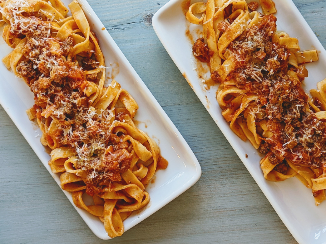 Two plates of fettuccine pasta with meat sauce and grated cheese on top.