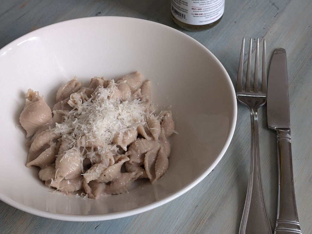A bowl of pasta topped with grated cheese on a wooden table.