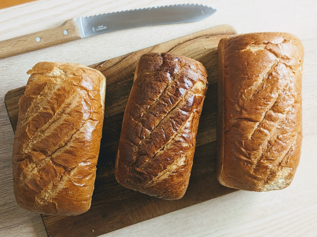 Three loaves of bread on a cutting board, ideal for French toast.