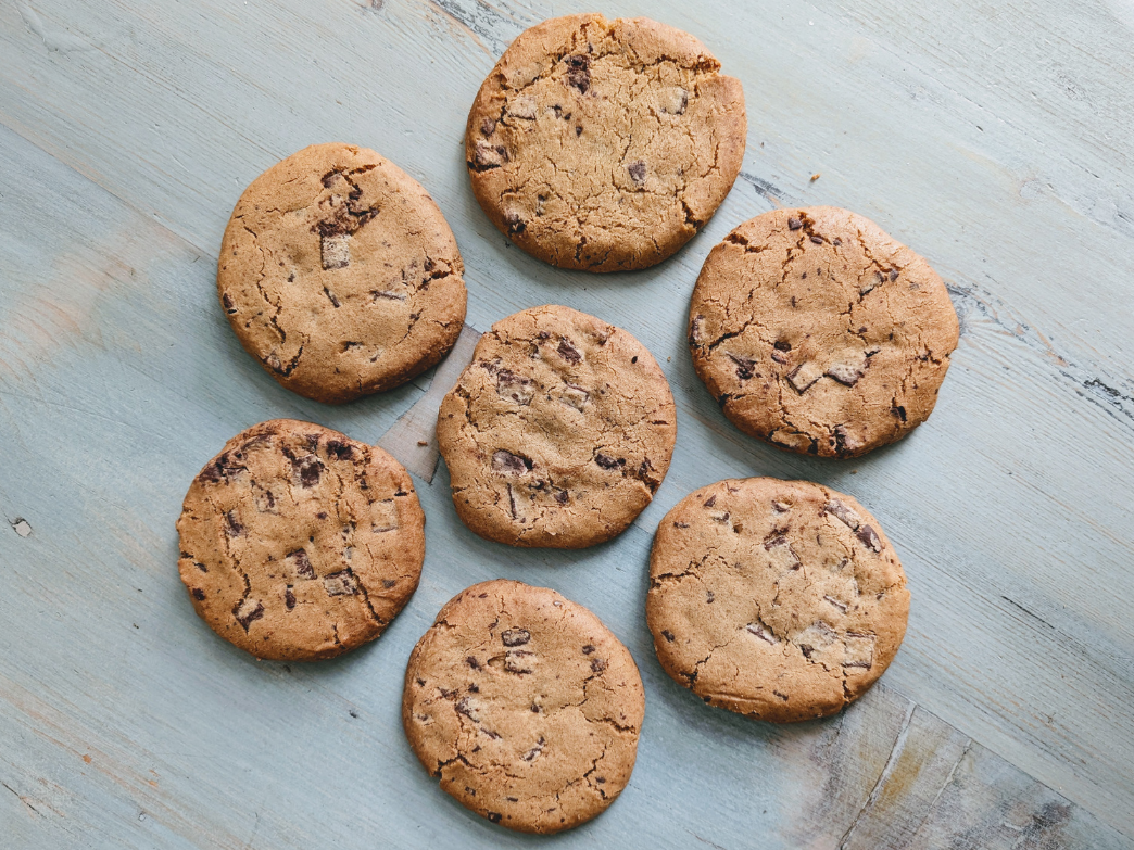 Seven chocolate chip cookies on a wooden surface
