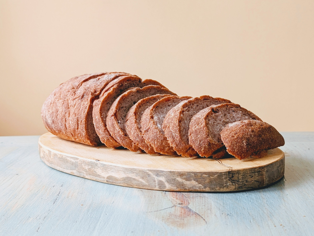 Front view of a sliced rustic brown loaf showing thick crust and interior on a round wooden board and pale blue table