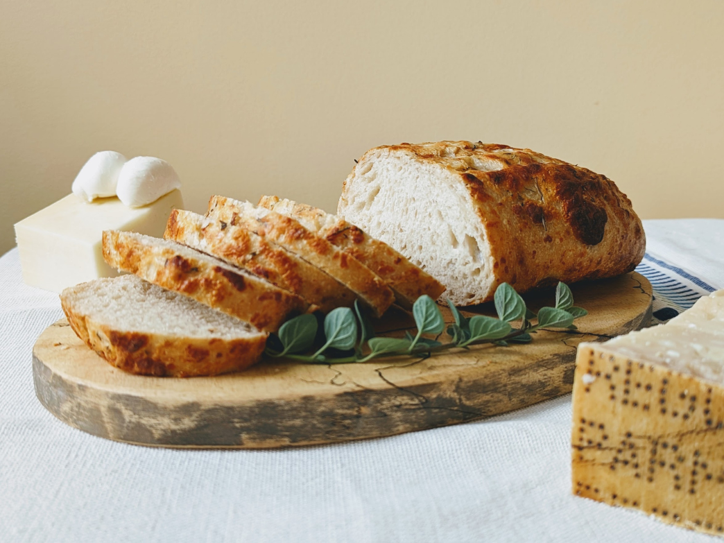 Sliced artisan bread on a wooden board with herbs and cheese