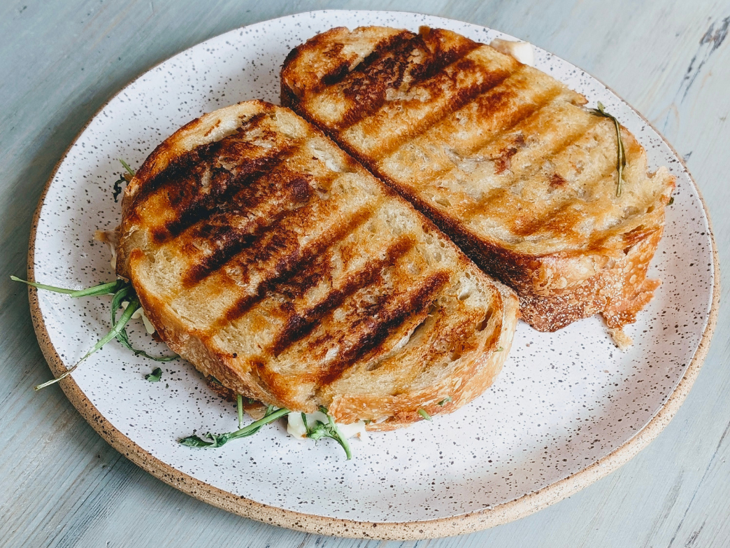 Toasted sourdough sandwich with arugula on a speckled ceramic plate, top-down on a light wood table