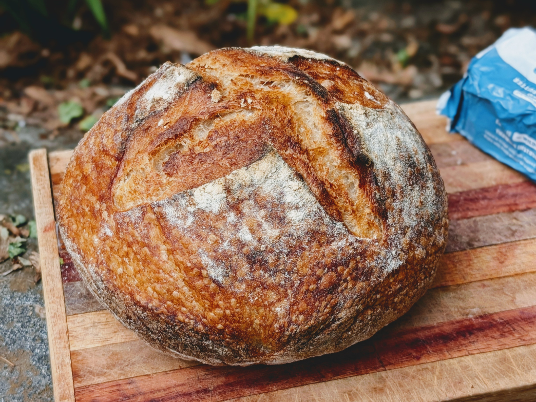 Round sourdough loaf with scored crust and flour dusting on a wooden cutting board