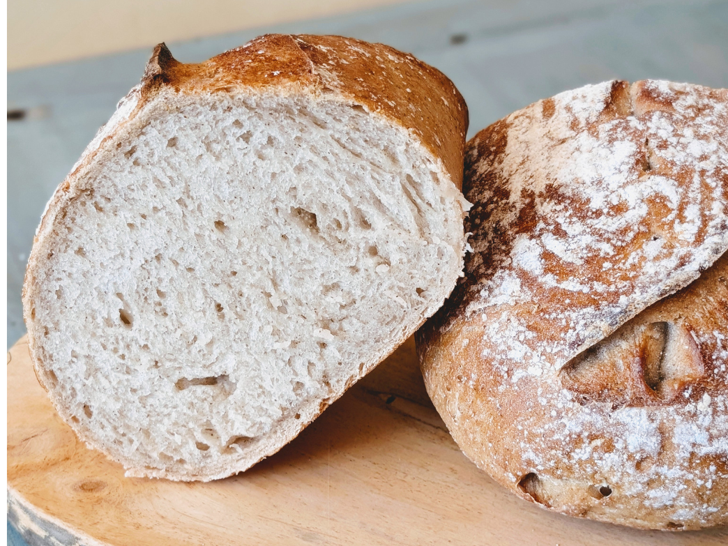 Two crusty artisan loaves on a wooden board, one sliced to show its airy interior and flour-dusted crust