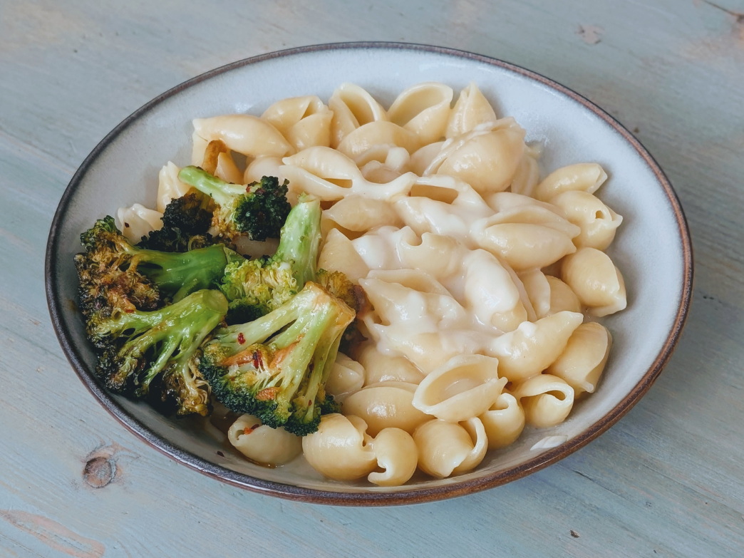 Bowl of shell pasta in creamy sauce with roasted broccoli florets on a wooden table