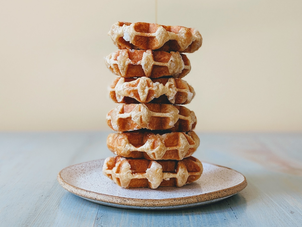Tall stack of round Belgian waffles with powdered sugar on a speckled ceramic plate
