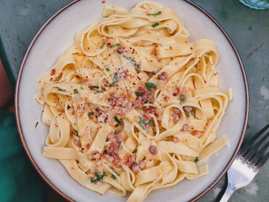 Creamy fettuccine with pancetta, chopped parsley and red pepper flakes on a white-rimmed plate