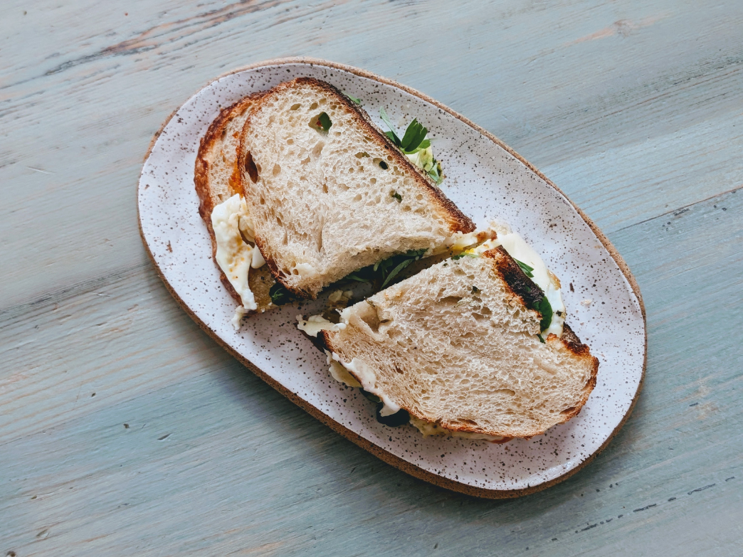 Two toasted sourdough sandwich halves with greens and melted cheese on a speckled oval plate on a light blue wooden table.