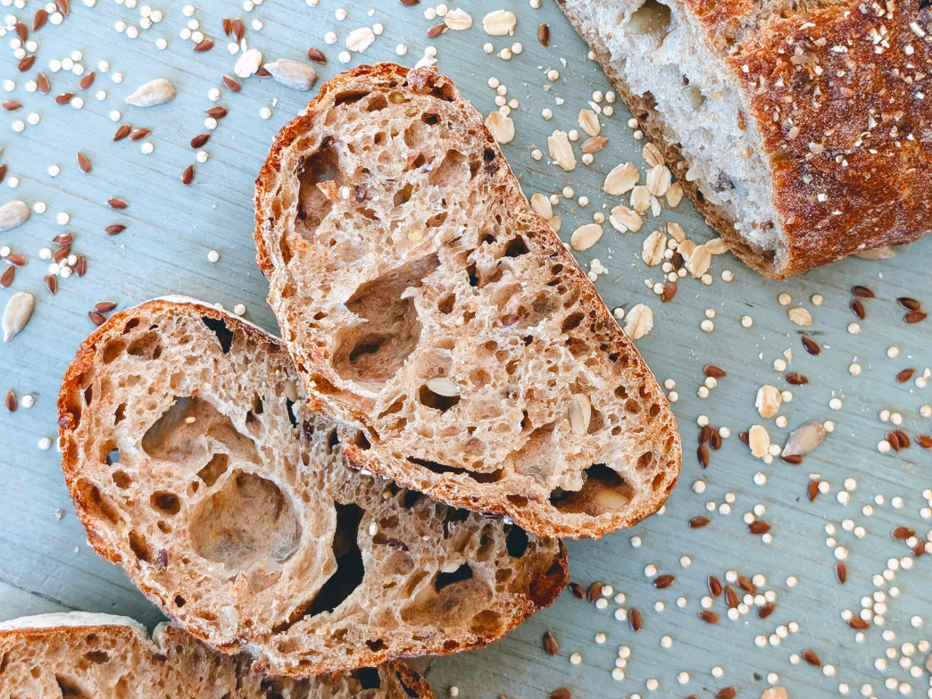 Sliced multigrain sourdough loaf with seeds and oats scattered on a blue board