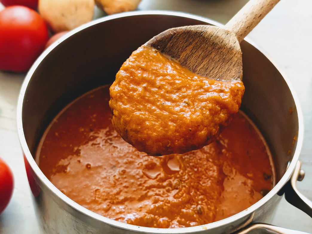 Wooden spoon lifting thick marinara-style tomato sauce from a stainless steel saucepan