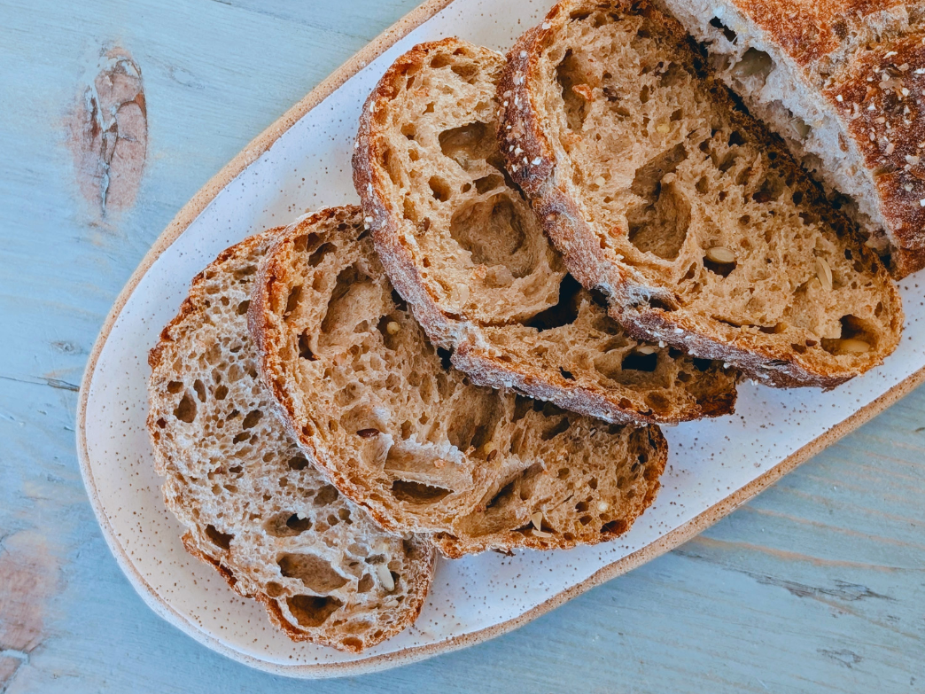 Overhead view of sliced seeded sourdough loaf on an oval speckled plate on a light blue wooden table