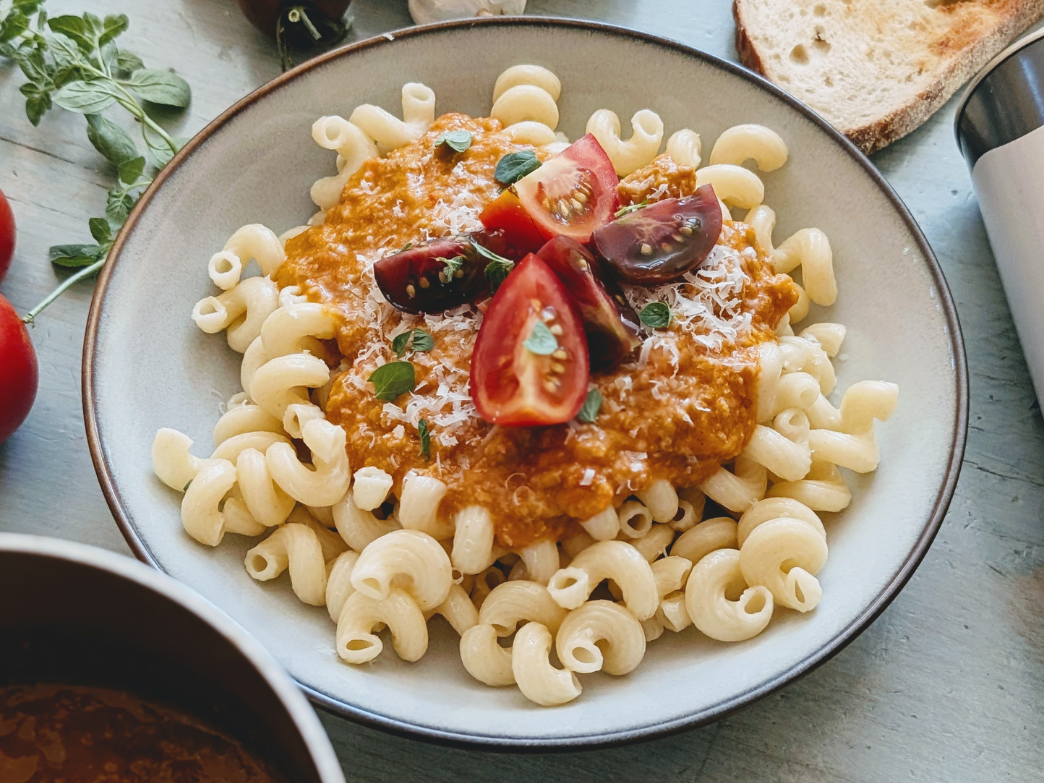 Plate of cavatappi pasta topped with tomato sauce, grated cheese, cherry tomato halves and basil on a rustic table