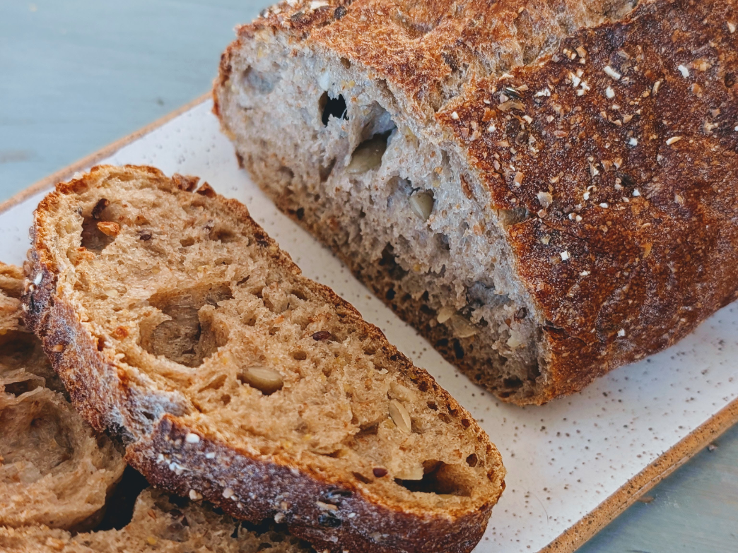 Close-up of sliced whole grain bread loaf showing crusty exterior, open crumb, and visible seeds on a speckled plate