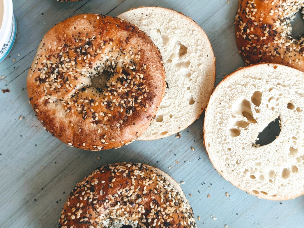 Top-down view of everything bagels, one sliced in half showing airy crumb on a light blue wooden surface
