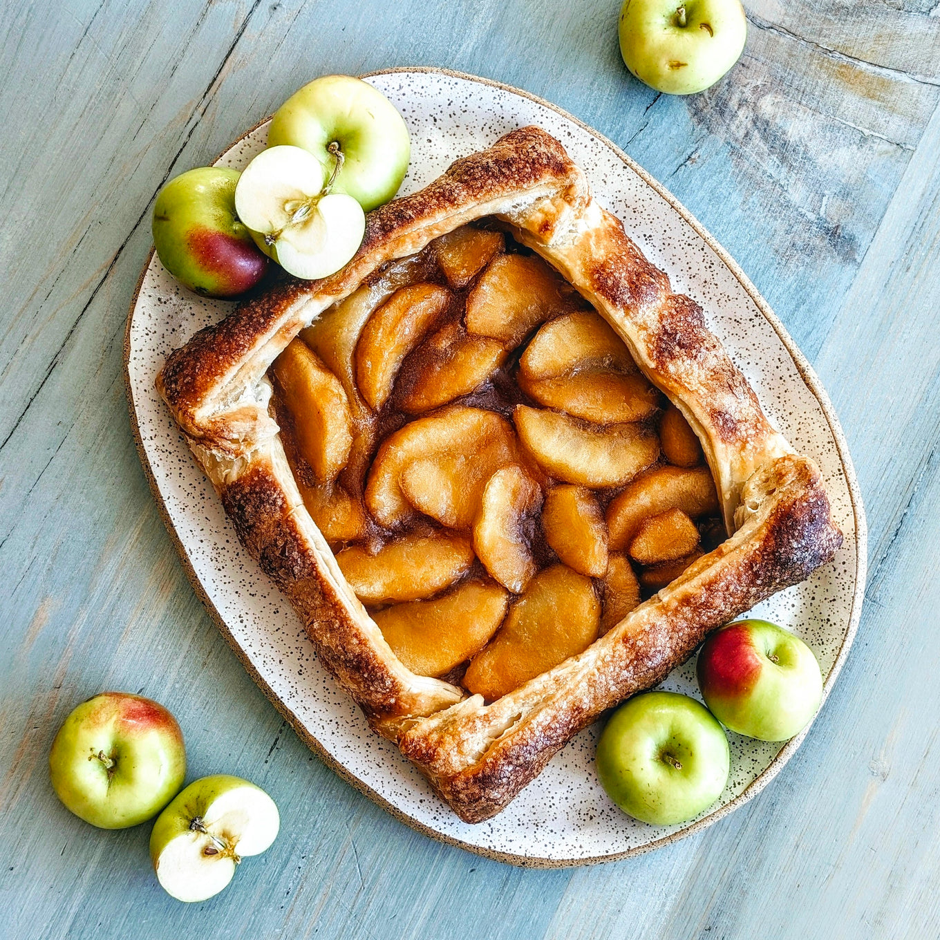 A square Apple Caramel Galette with sliced apples and a golden crust, surrounded by green and red apples.
