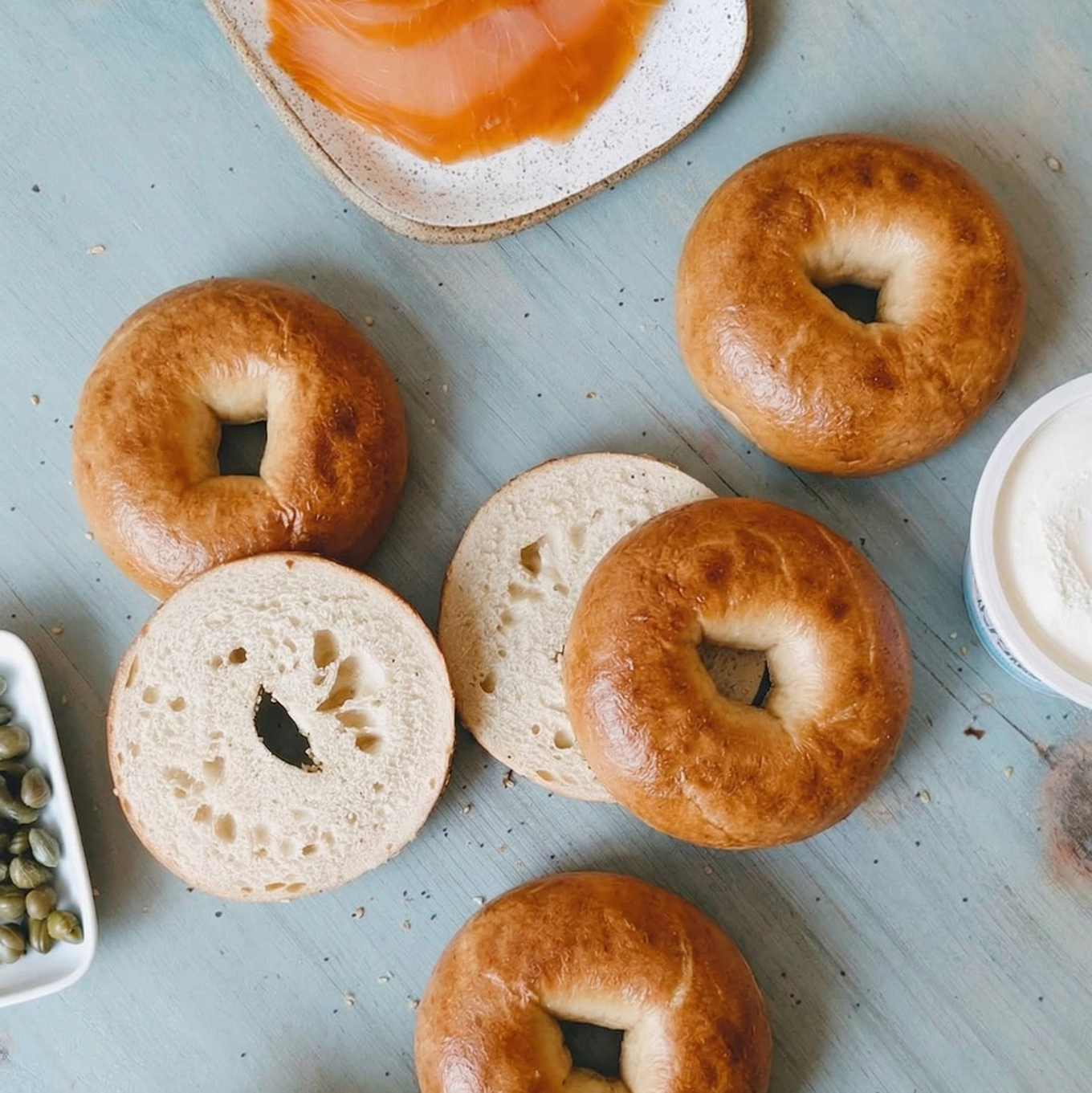 Overhead of New York plain bagels (4-pack) showing golden crust and one sliced bagel with cream cheese