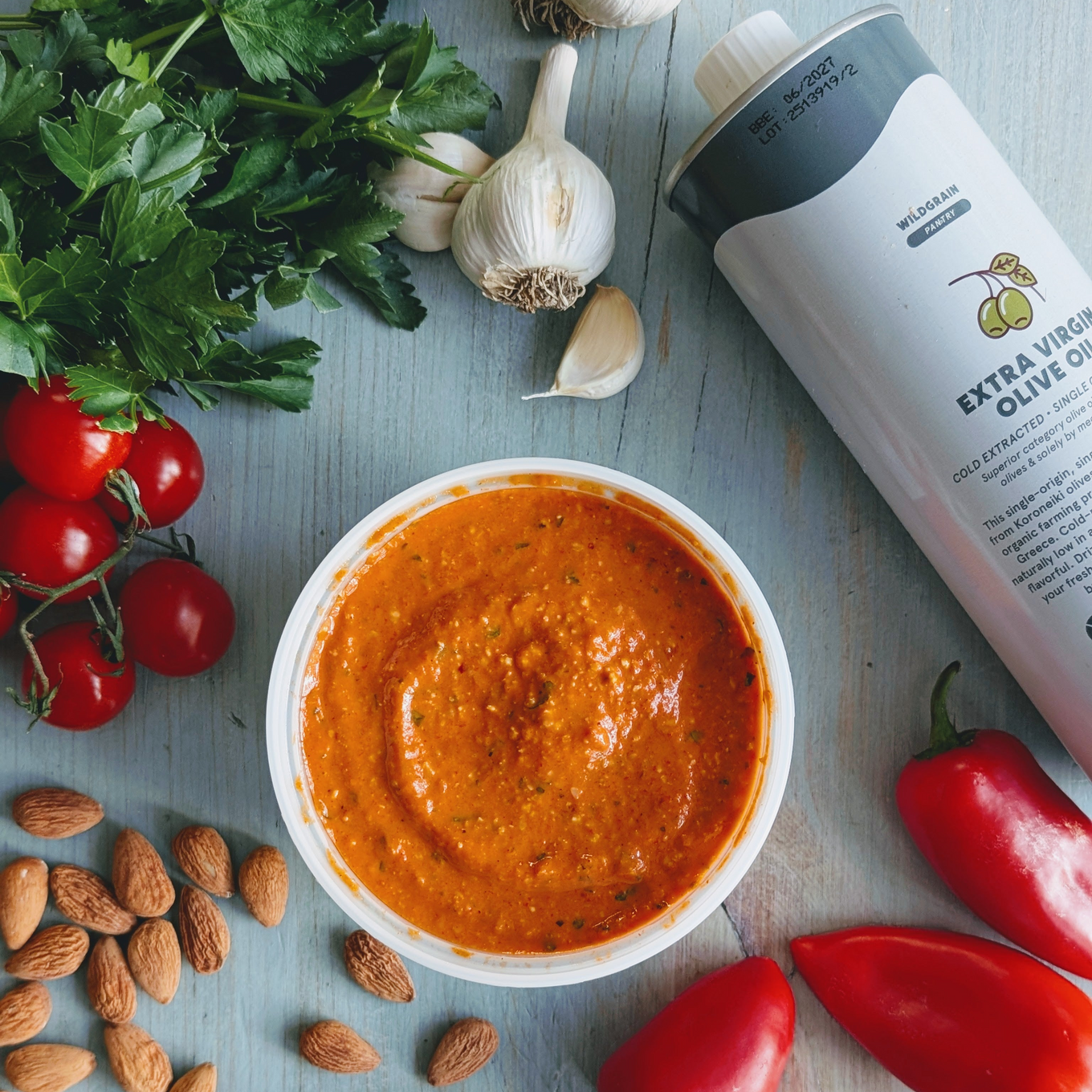 Romesco sauce in a bowl with almonds, garlic, cherry tomatoes, parsley, and a can labeled EXTRA VIRGIN OLIVE OIL