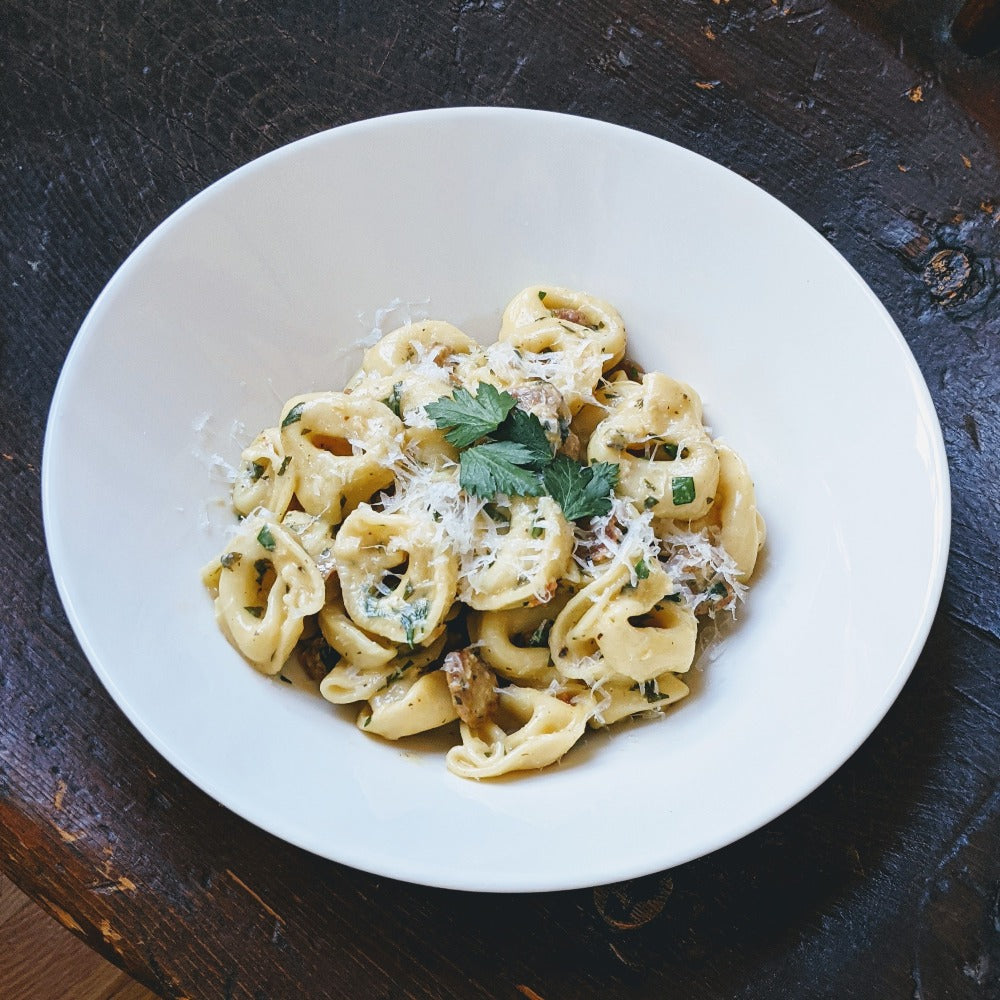Tortellini with grated Parmesan and parsley in a white bowl on dark wooden table
