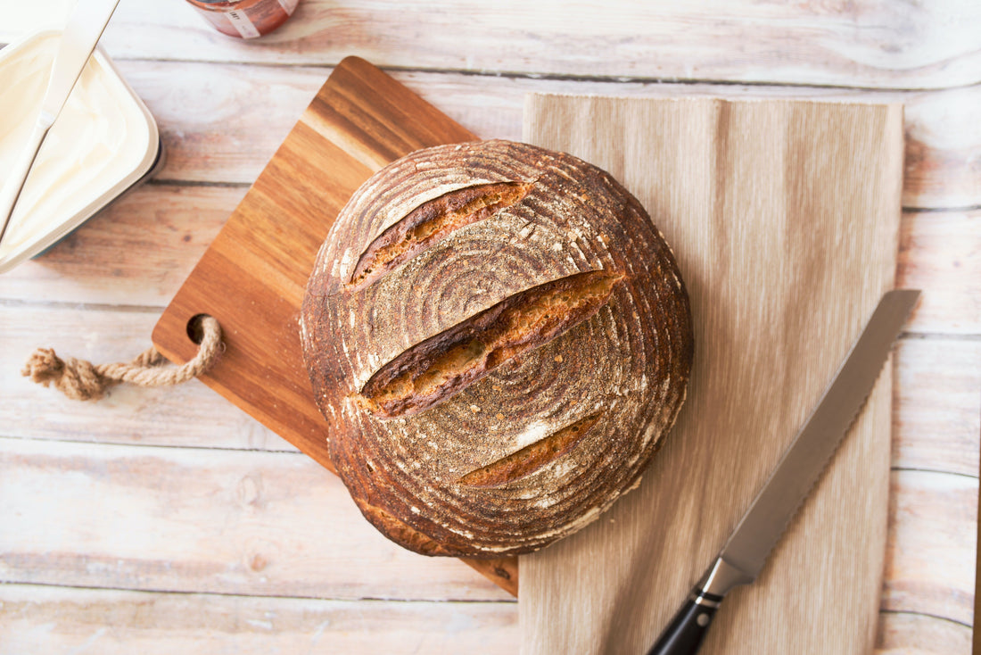 A round loaf of sourdough bread on a wooden cutting board with a knife and butter spread.