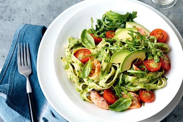A plate of avocado pesto pasta with cherry tomatoes and basil leaves