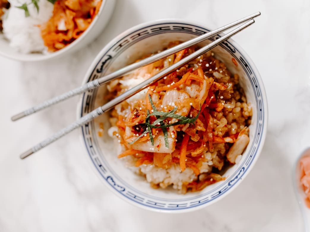 Bowl of rice topped with kimchi and carrots, chopsticks resting on the side