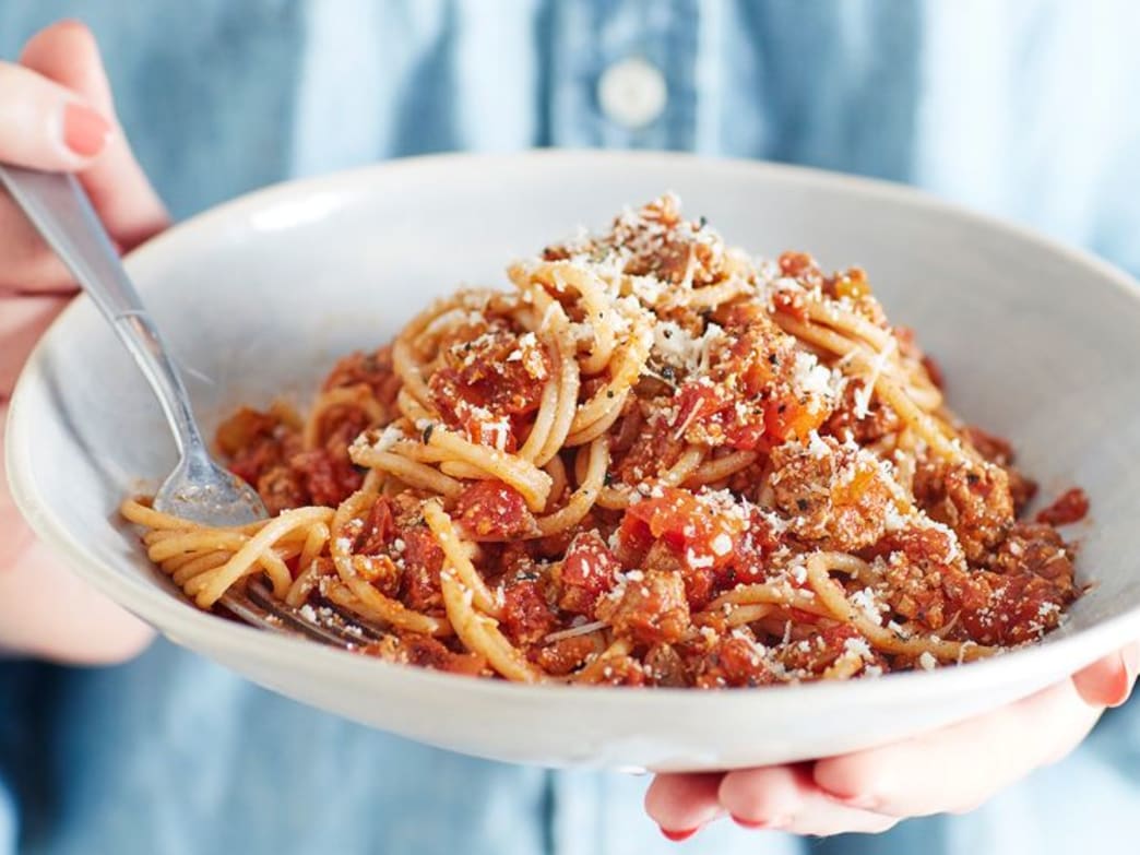 A bowl of turkey spaghetti bolognese topped with grated cheese, held by a person.